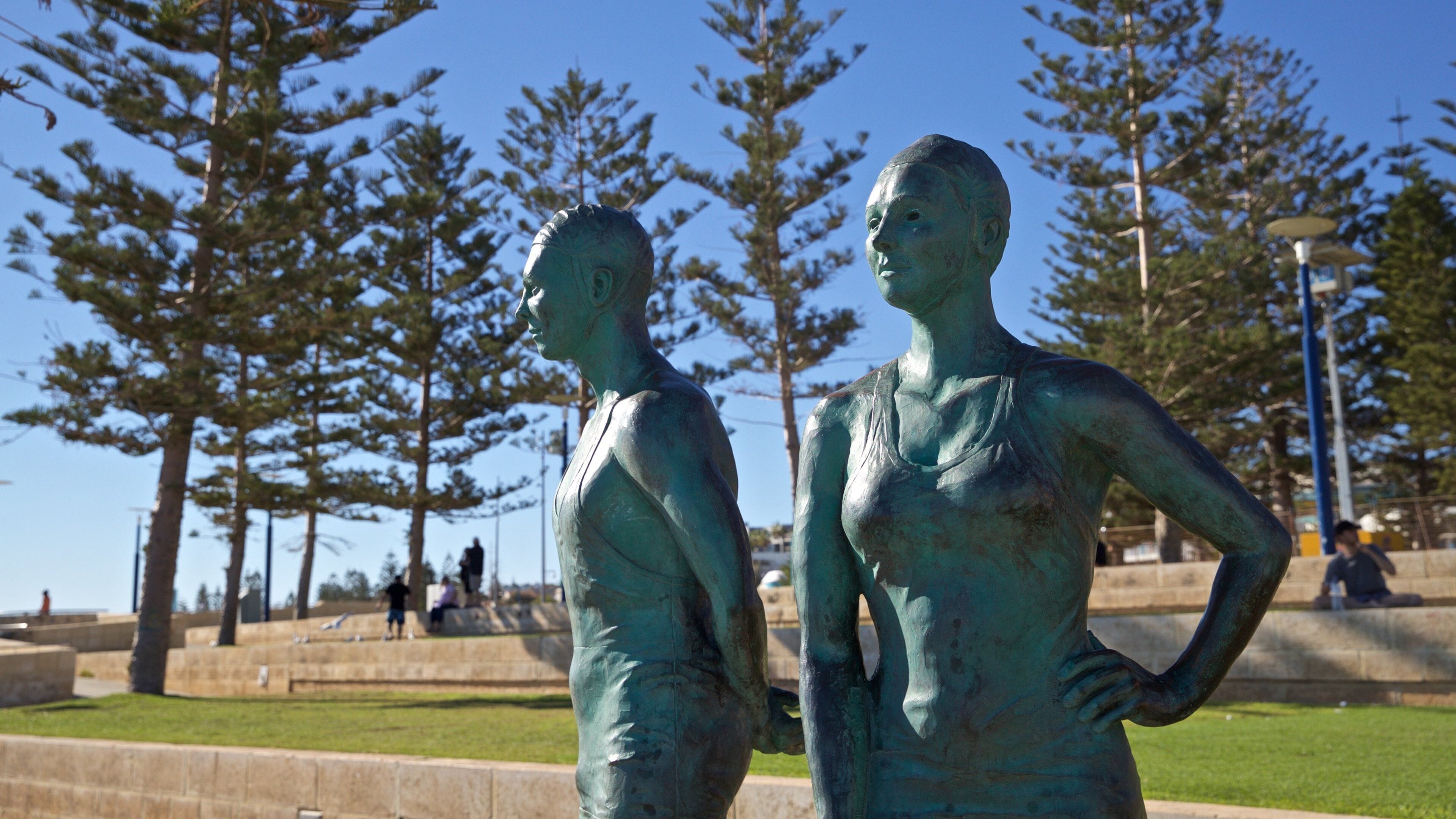 Two bronze statues of a man and a woman in a park with trees and a clear sky.
