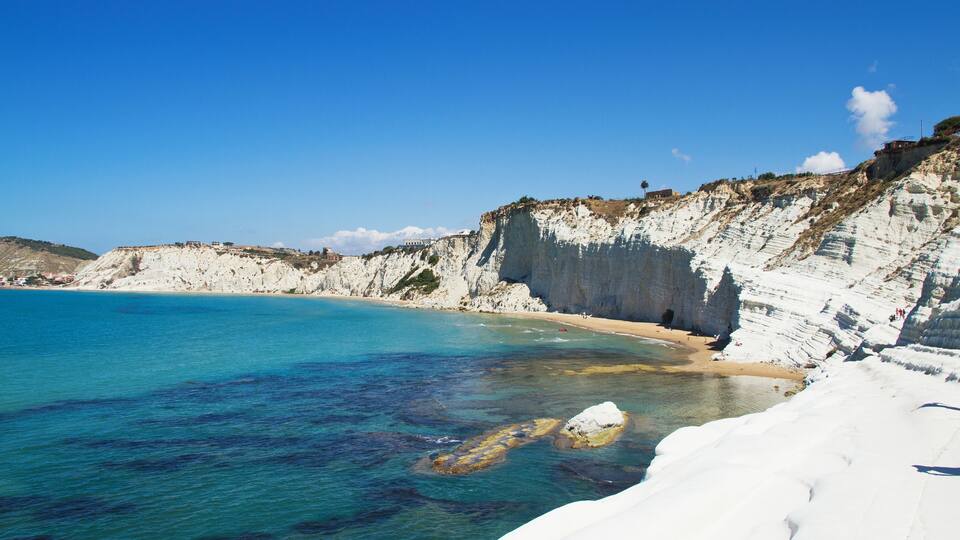 A coastal landscape with white cliffs, clear turquoise waters, and a sandy beach.