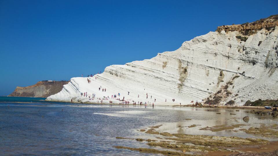 A coastal cliff with people on it and a beach in the foreground.
