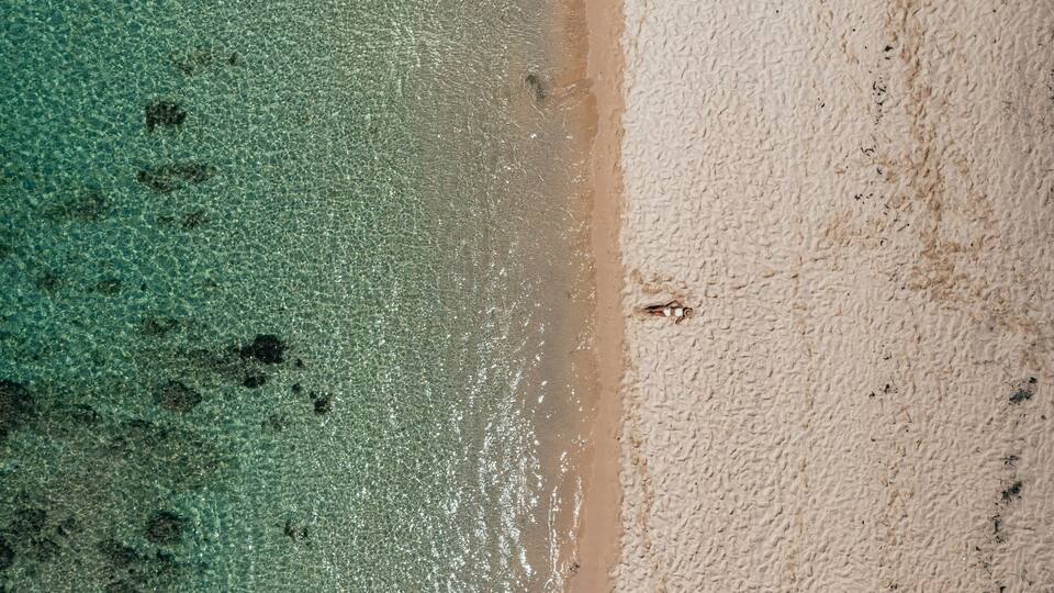 An aerial view of a beach with clear turquoise water and a sandy shore.