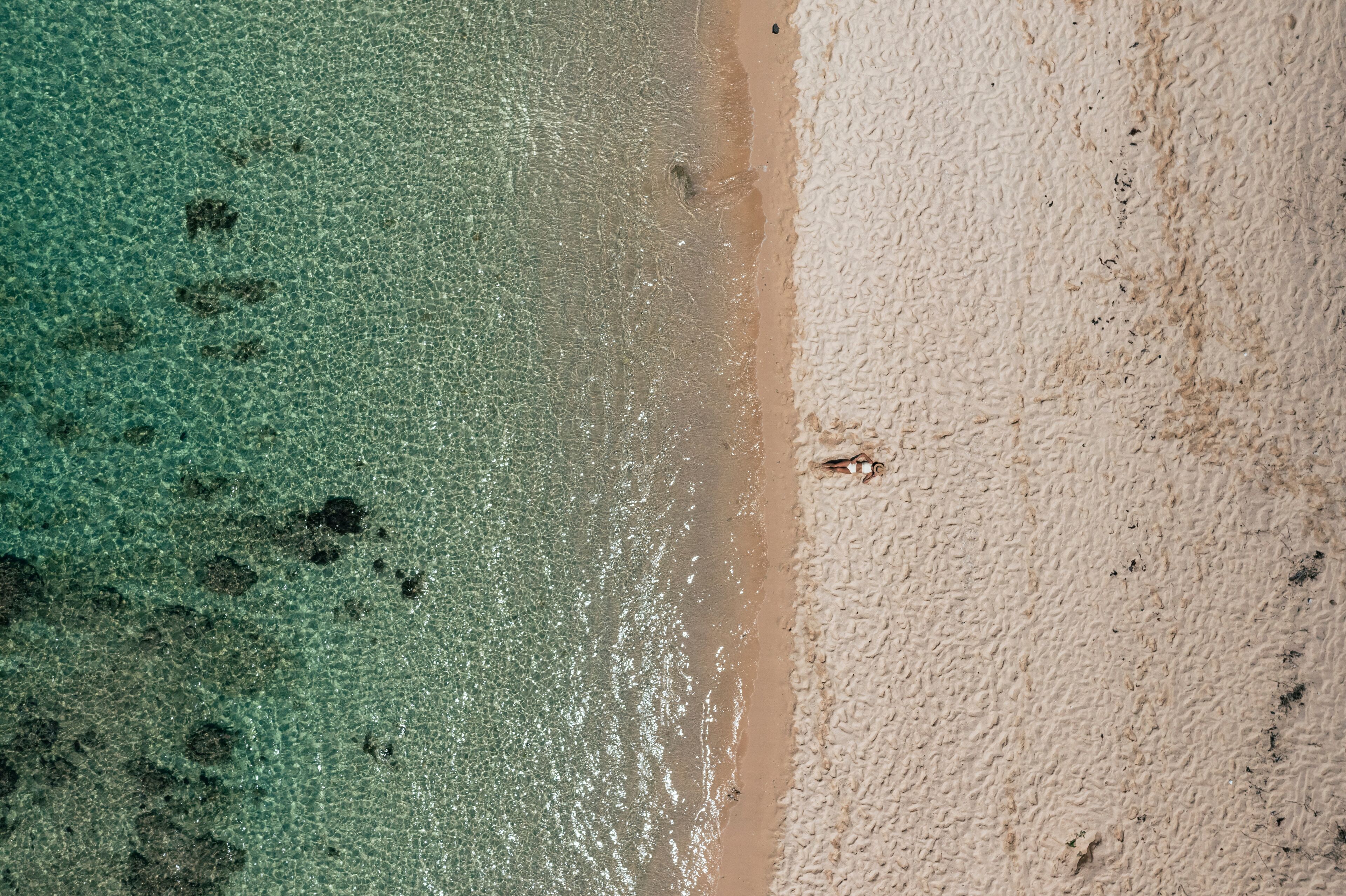 An aerial view of a beach with clear turquoise water and a sandy shore.