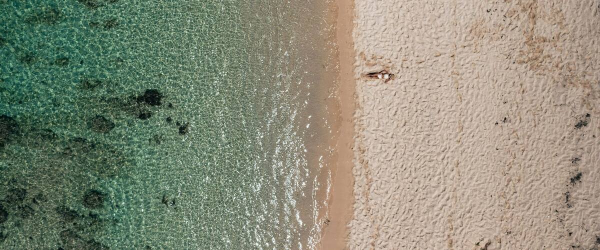 An aerial view of a beach with clear turquoise water and a sandy shore.