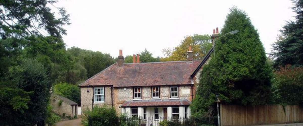 A traditional stone house with a tiled roof, surrounded by a grassy yard and a wooden fence.
