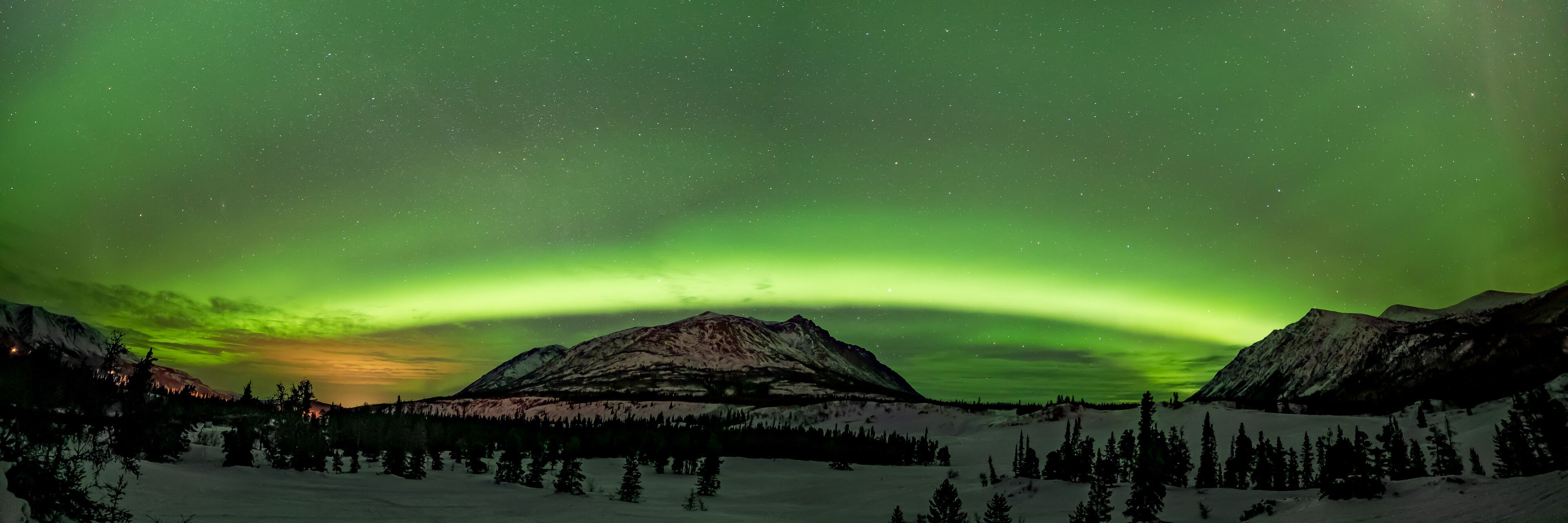 Incredible green aurora borealis seen across the Carcross Desert in northern Canada during winter time with northern lights in panorama, panoramic snow capped winter sky scenic view.