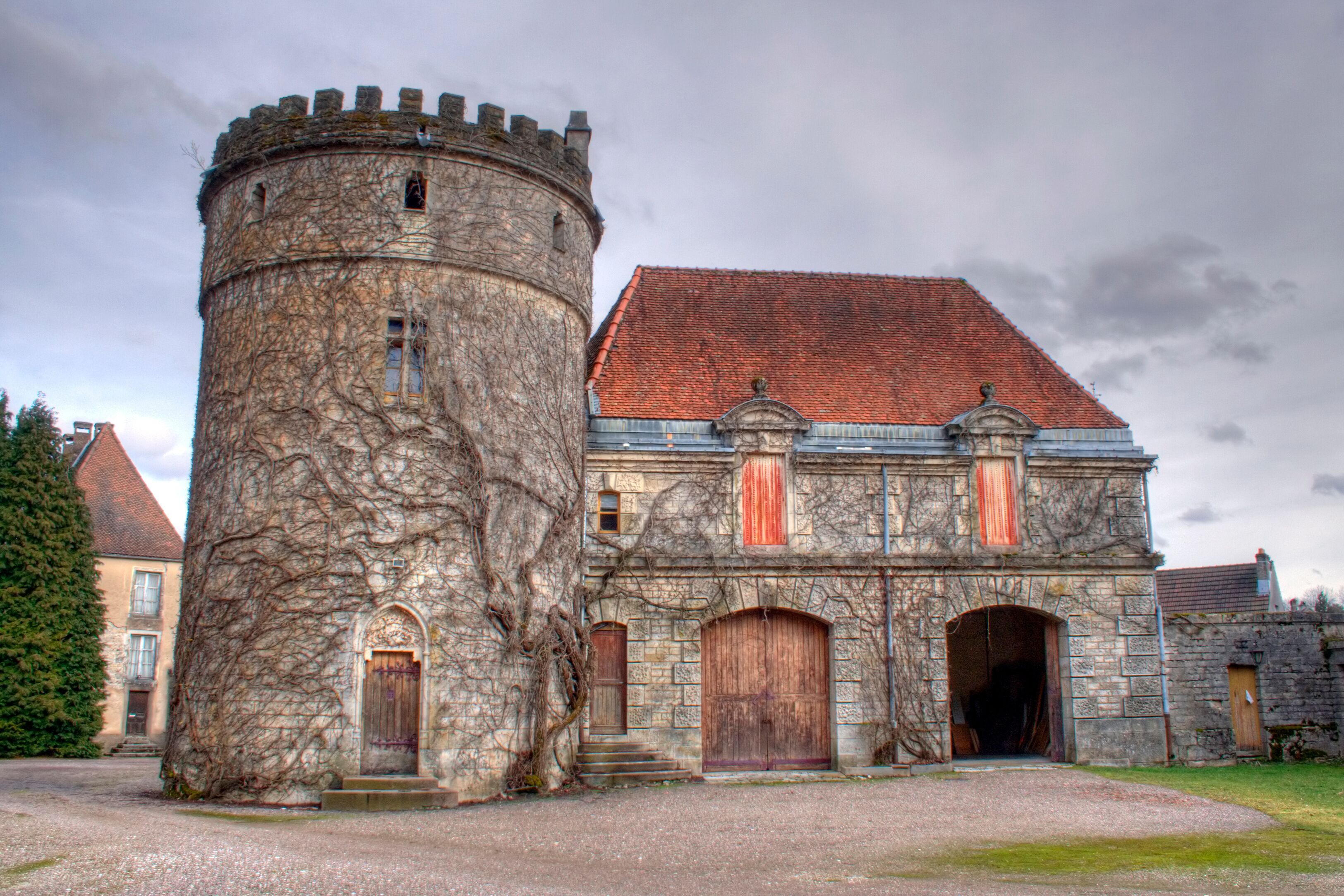 A historic stone building with a tower, red-tiled roof, and wooden doors.