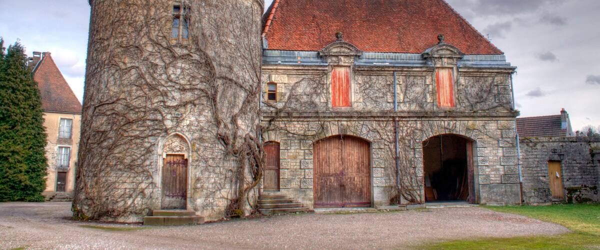 A historic stone building with a tower, red-tiled roof, and wooden doors.