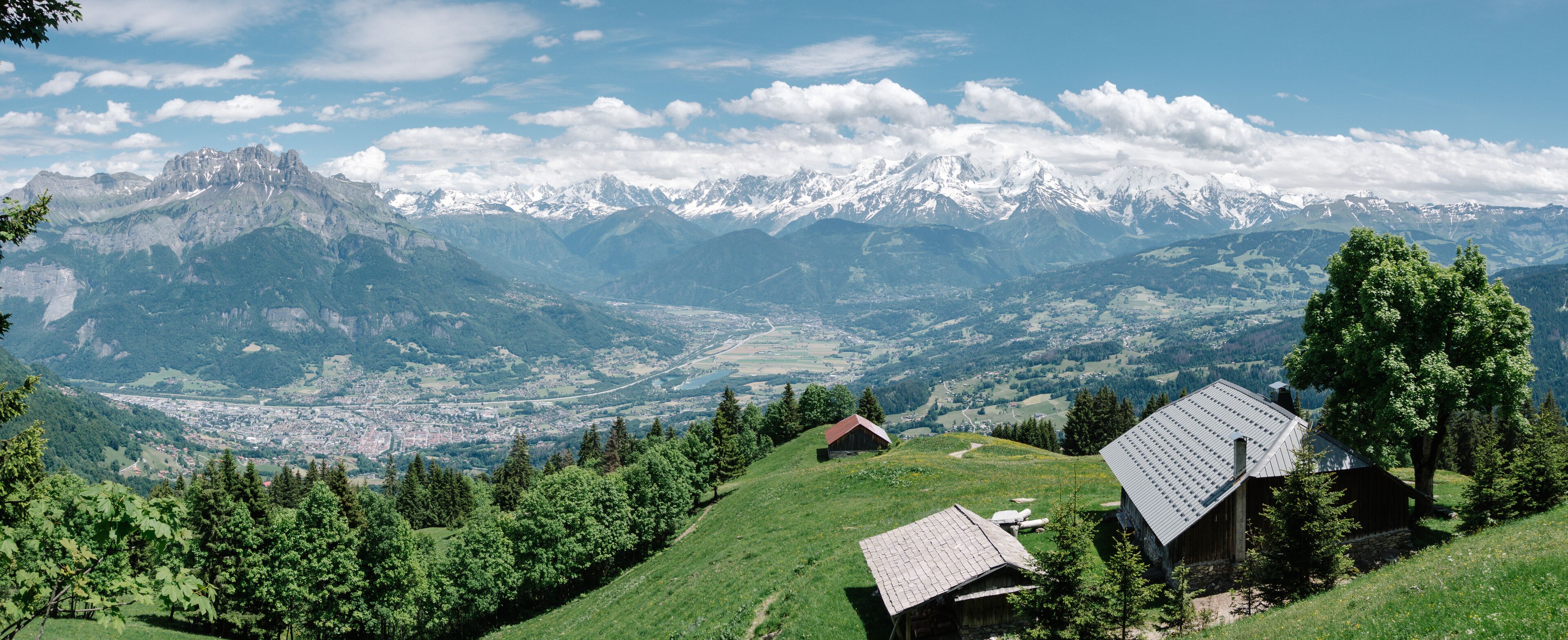A mountainous landscape with snow-capped peaks, a valley with a town, and wooden houses on a hillside.