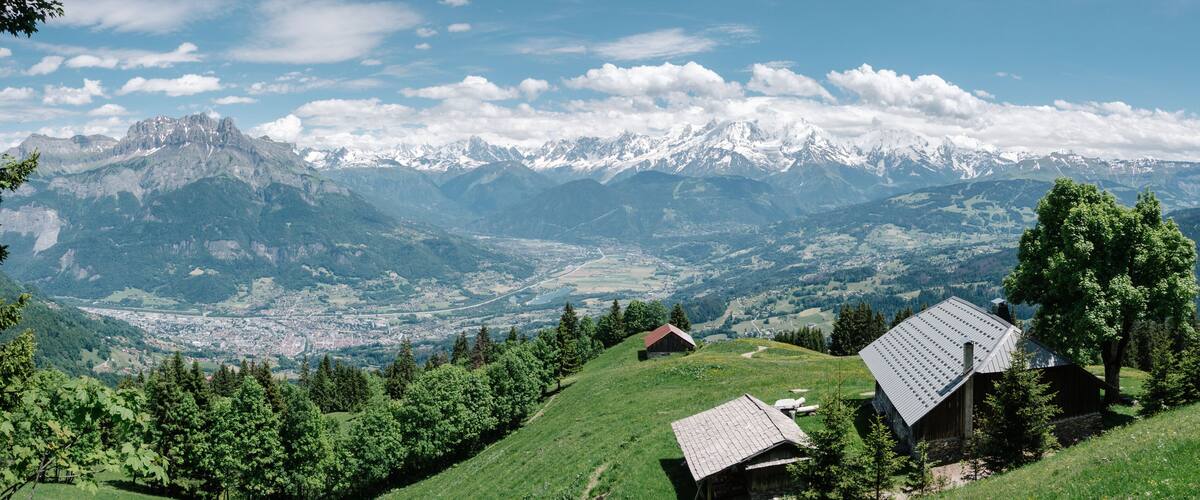 A mountainous landscape with snow-capped peaks, a valley with a town, and wooden houses on a hillside.