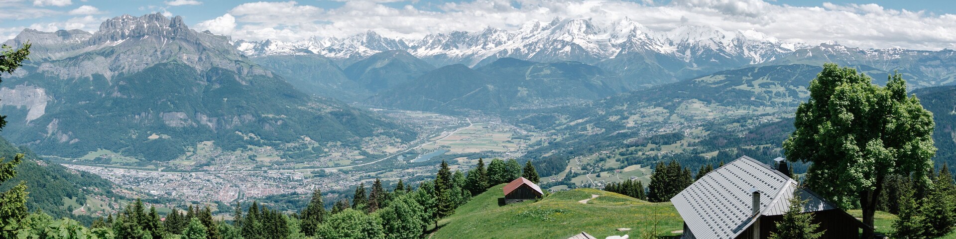 A mountainous landscape with snow-capped peaks, a valley with a town, and wooden houses on a hillside.