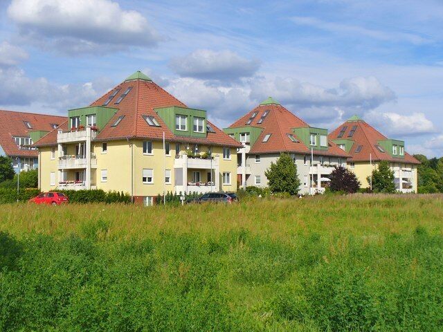 A residential building complex with multiple apartment buildings, green roofs, and a grassy field in the foreground.
