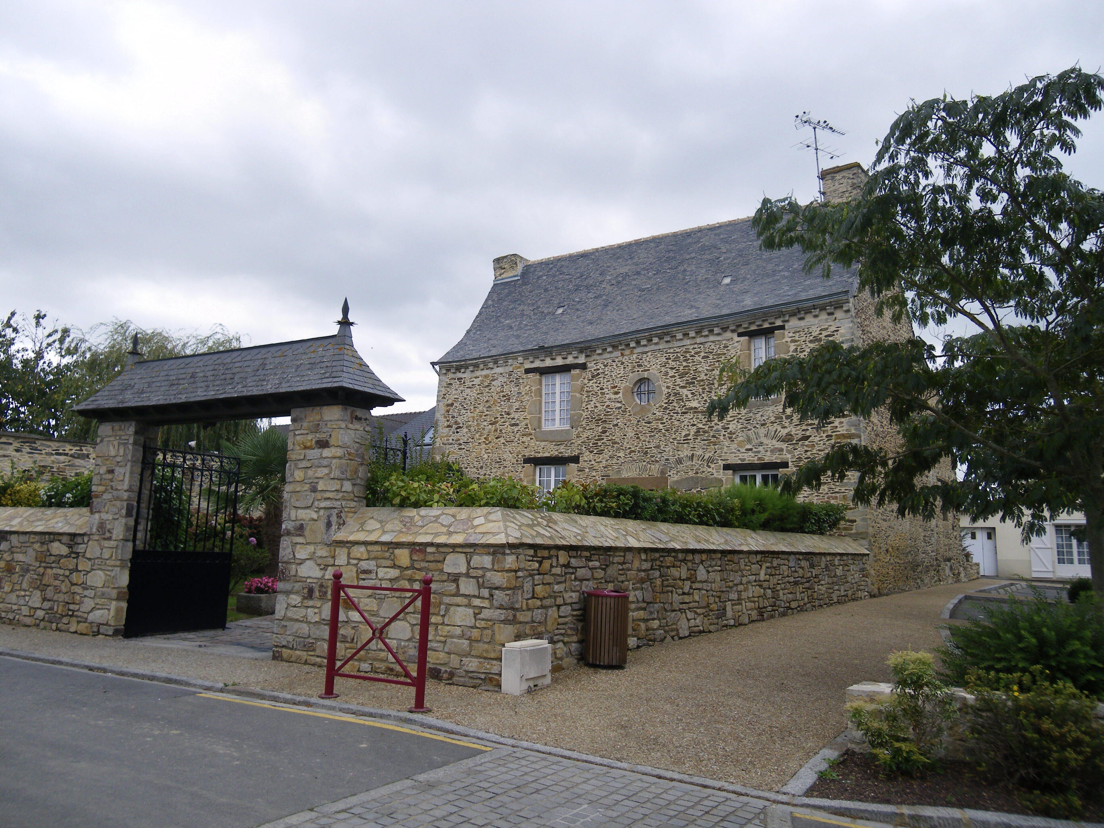 A stone building with a gated entrance, surrounded by gravel and greenery.