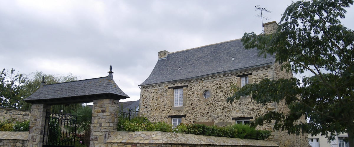 A stone building with a gated entrance, surrounded by gravel and greenery.