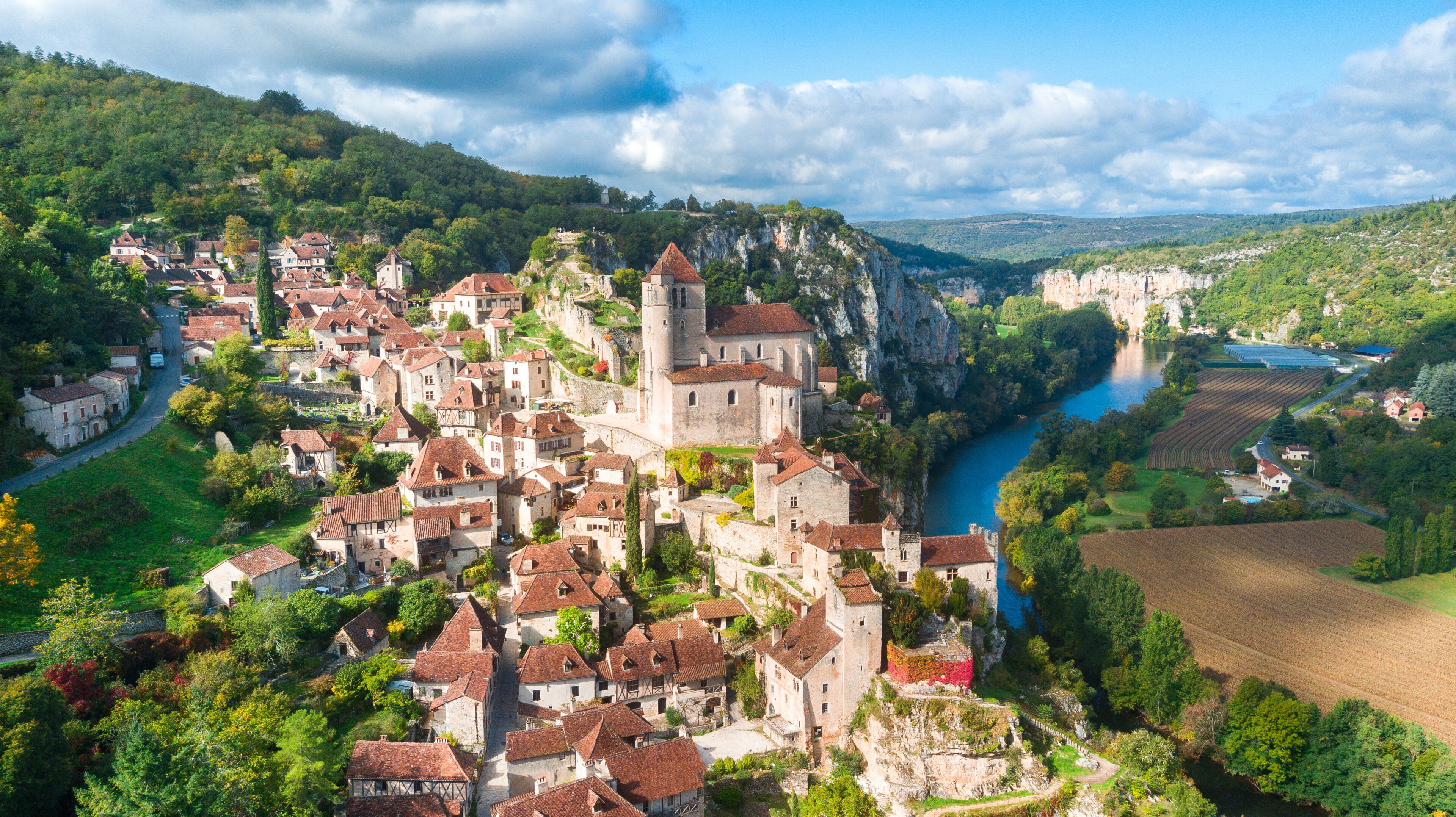 A medieval town with a river, surrounded by hills and greenery.