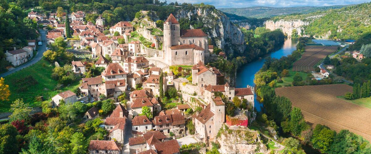 A medieval town with a river, surrounded by hills and greenery.