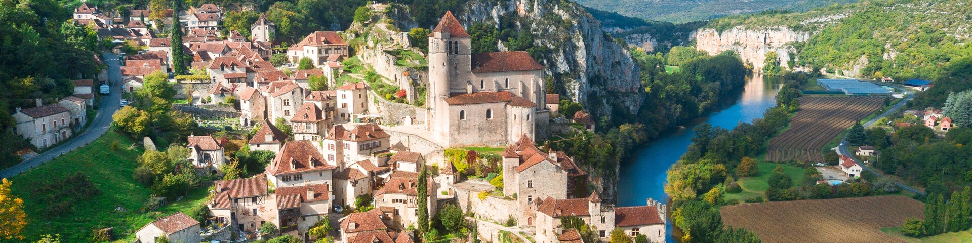 A medieval town with a river, surrounded by hills and greenery.