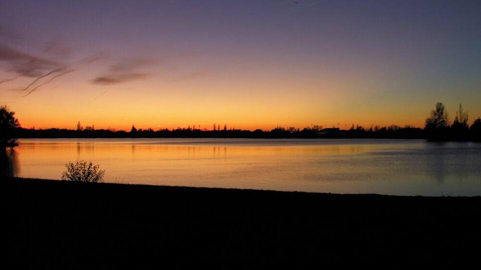 A sunset over a calm lake with a silhouette of trees and a distant city skyline.