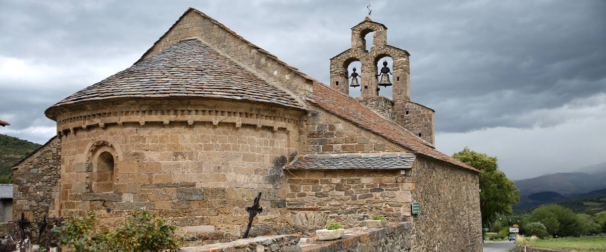 A stone church with a bell tower and a circular apse.