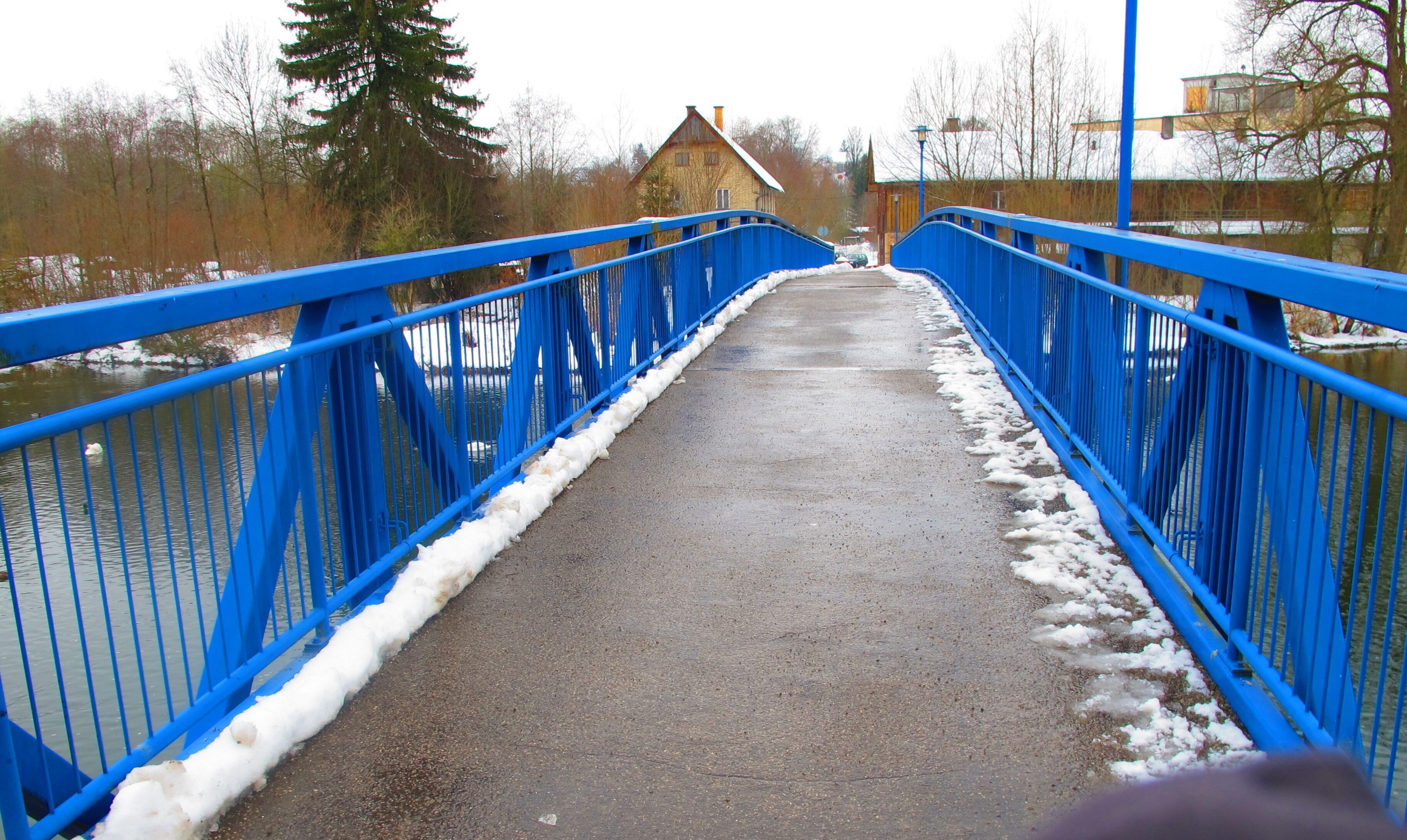 A blue bridge over a river with snow on the edges.