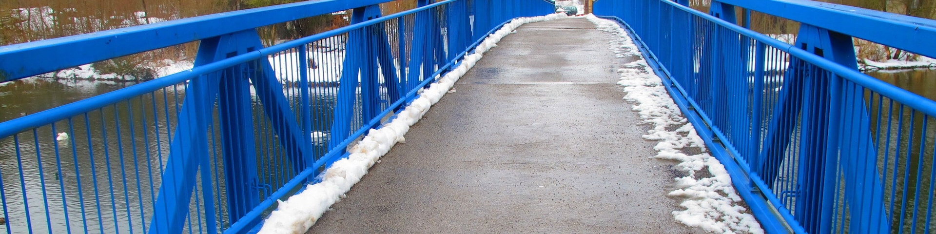 A blue bridge over a river with snow on the edges.