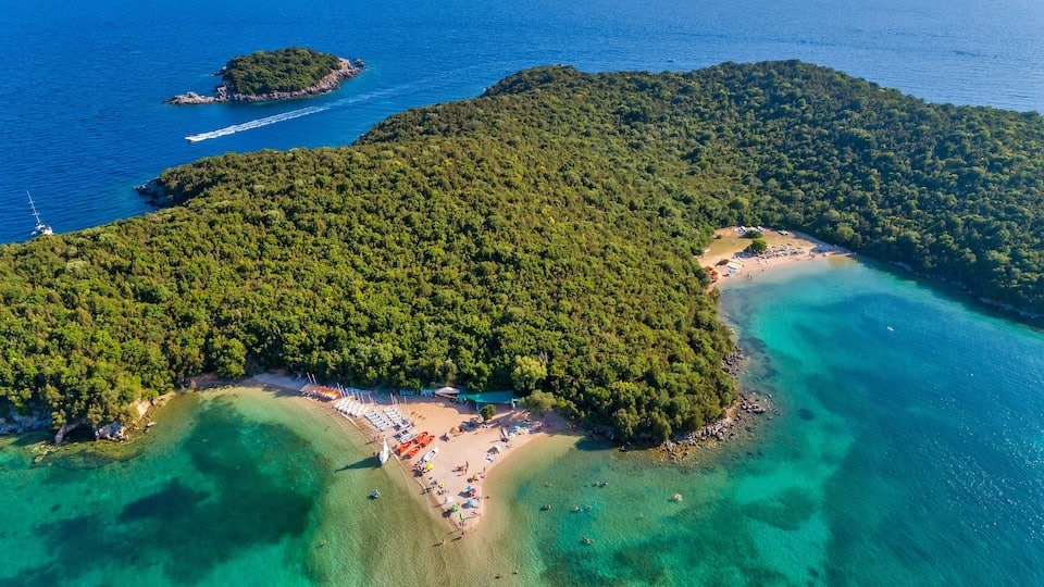 An aerial view of a tropical island with a beach, clear turquoise waters, and lush greenery.