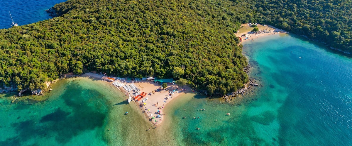 An aerial view of a tropical island with a beach, clear turquoise waters, and lush greenery.
