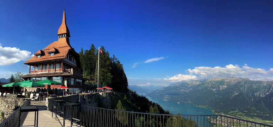 A mountain lodge with a steep roof and a tall tower, overlooking a valley and lake.