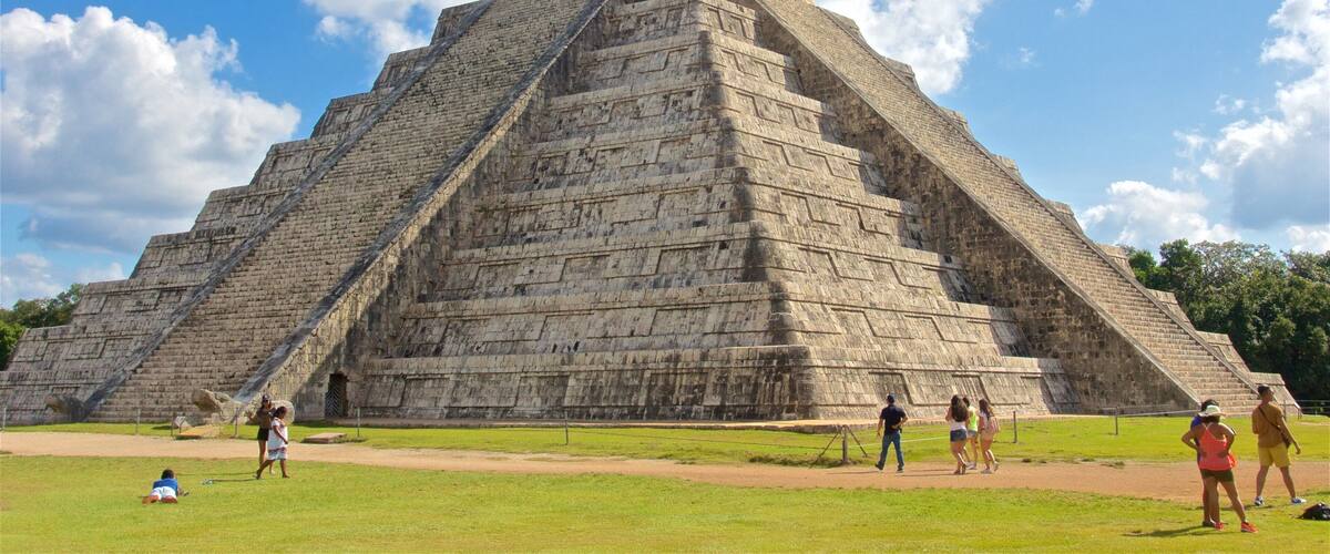A large stone pyramid with a flat top, surrounded by a grassy area with people walking around.