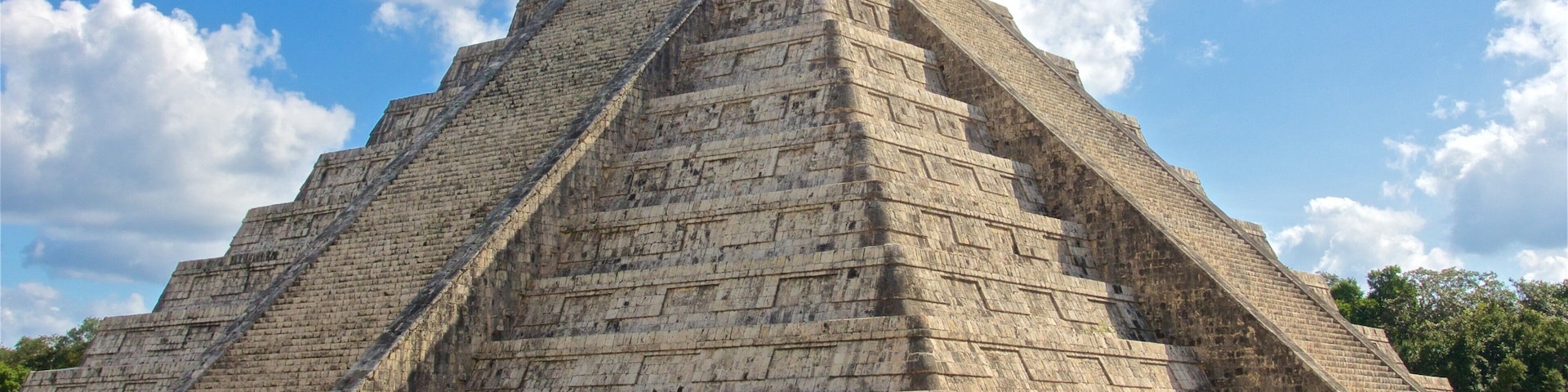 A large stone pyramid with a flat top, surrounded by a grassy area with people walking around.