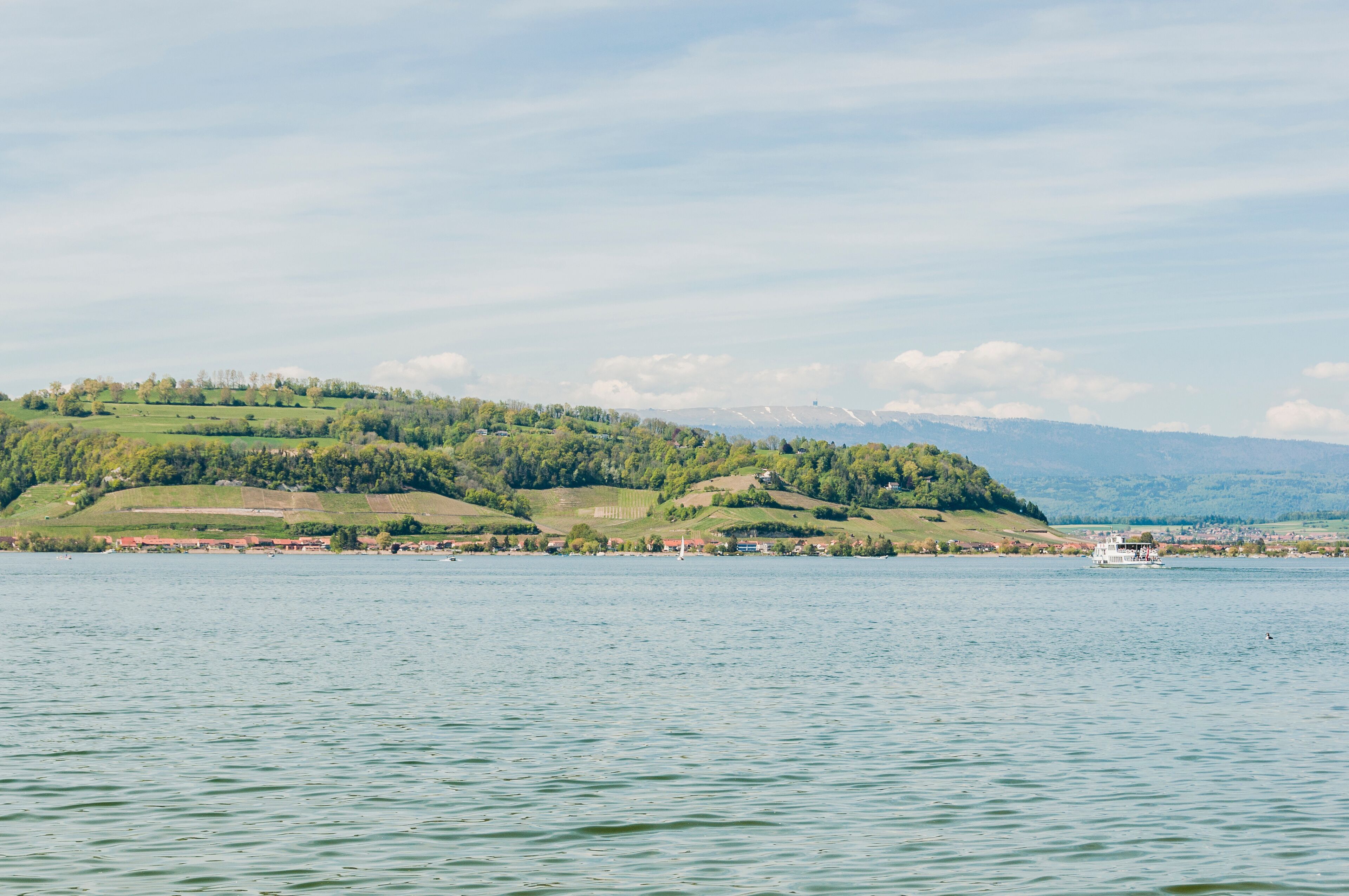 A calm lake with a boat, green hills, and a distant mountain range.