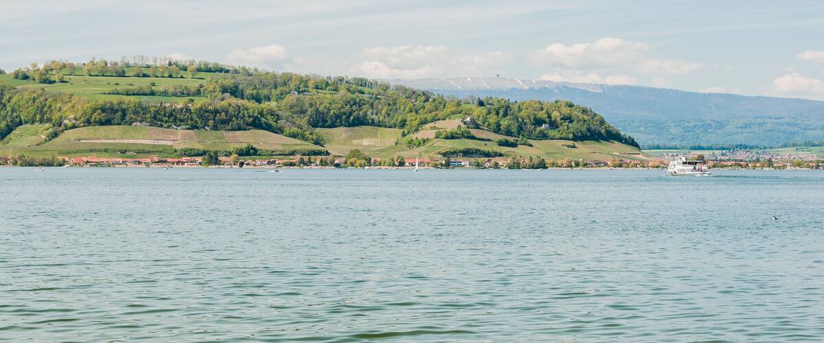 A calm lake with a boat, green hills, and a distant mountain range.