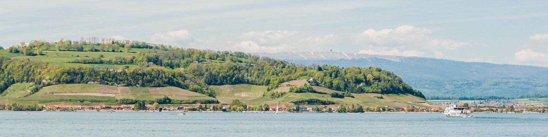 A calm lake with a boat, green hills, and a distant mountain range.