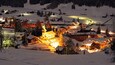 A snow-covered village at night with illuminated buildings and a church.