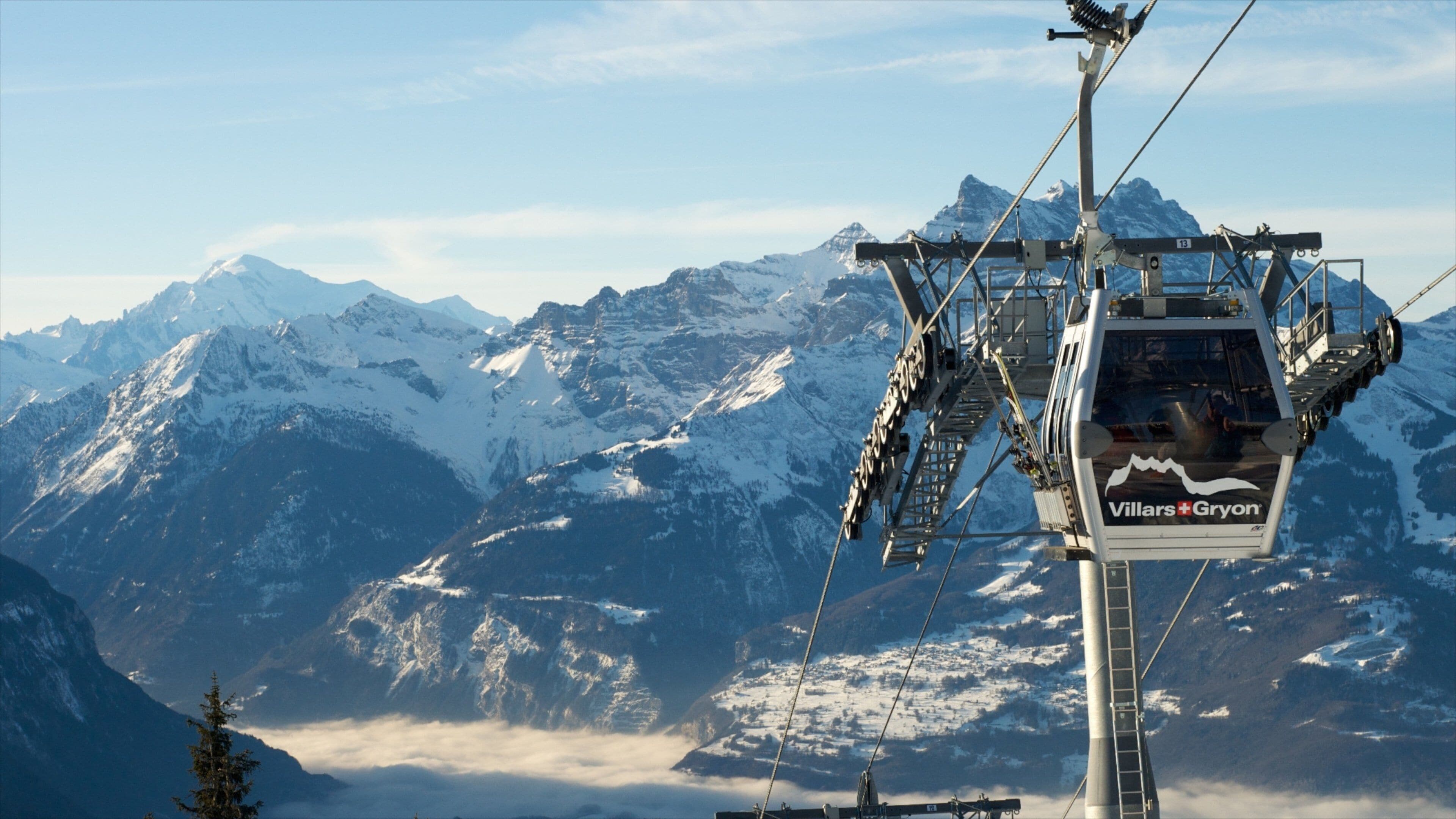 A chairlift with 'Villars-Gryon' branding, snow-covered mountains, and a forested valley in the background.