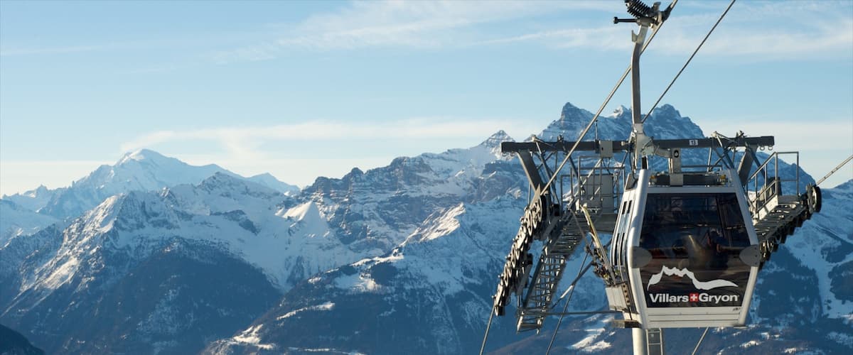A chairlift with 'Villars-Gryon' branding, snow-covered mountains, and a forested valley in the background.