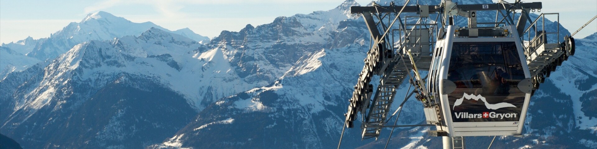 Un telesilla con la marca 'Villars-Gryon', montañas nevadas y un valle boscoso al fondo.