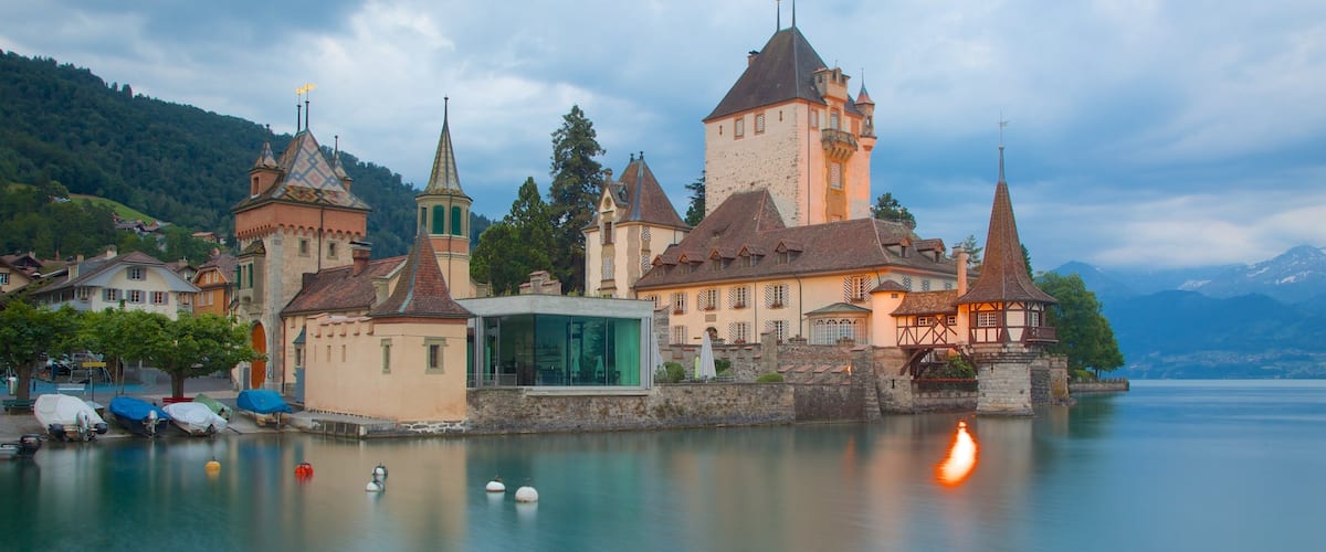 A historic castle by a calm lake with boats docked nearby.