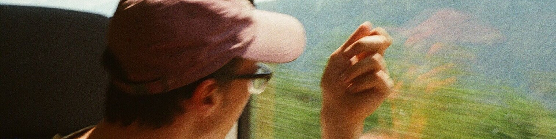 Una persona con gorra y gafas observa un paisaje montañoso desde una ventana.