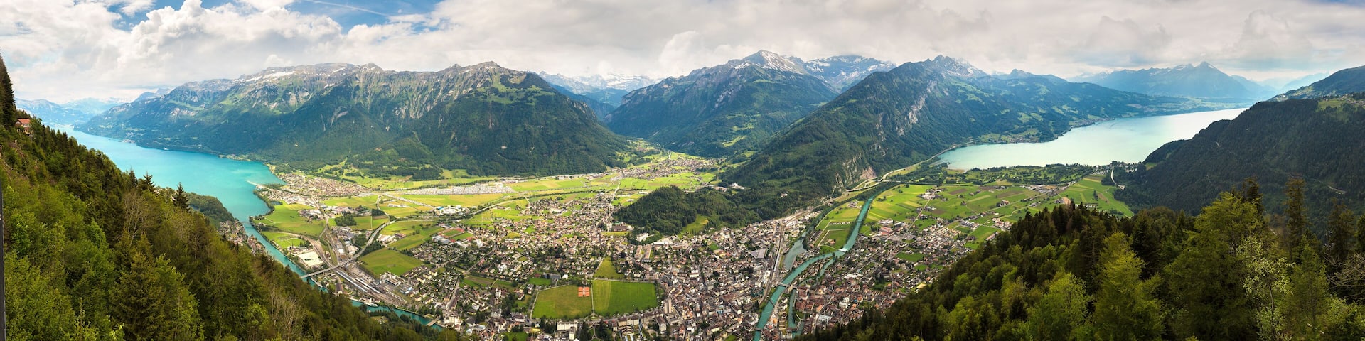 A mountainous landscape with a town nestled in a valley, surrounded by lush greenery and a turquoise lake.