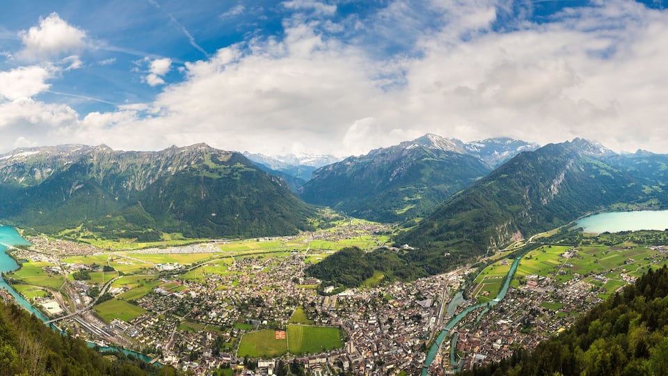 A mountainous landscape with a town nestled in a valley, surrounded by lush greenery and a turquoise lake.