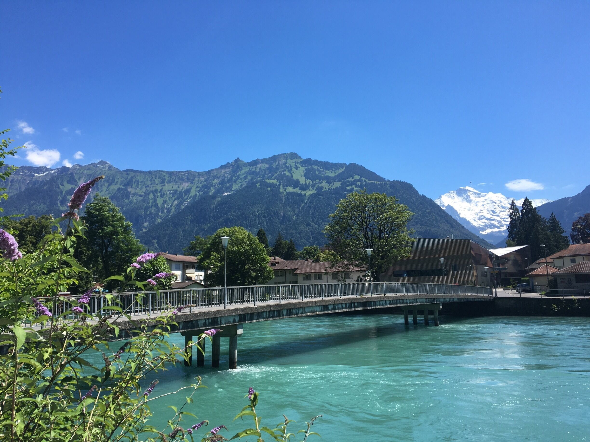 A bridge over a turquoise river with mountains in the background.