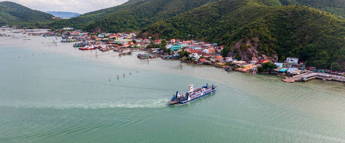 A coastal town with a large blue ferry, surrounded by lush green hills and a calm sea.