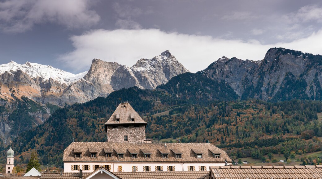 panorama view of snow-capped mountain peaks and fall foliage color forest in the Maienfeld region of Switzerland with the Brandis Castle and village roofs in the foreground