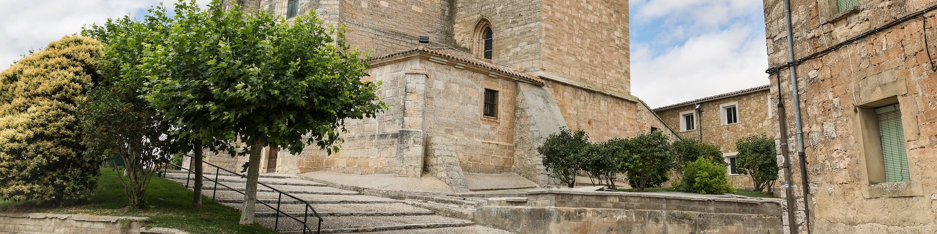 A historic stone building with a bell tower, surrounded by trees and a clear sky.