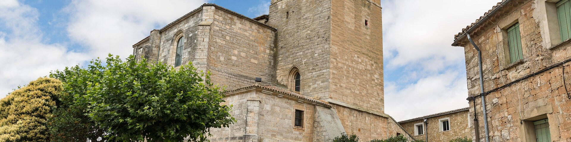Um edifício histórico de pedra com uma torre de sino, rodeado por árvores e um céu limpo.