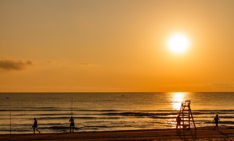 Ein Strand bei Sonnenuntergang, Menschen laufen und spielen am Wasser.