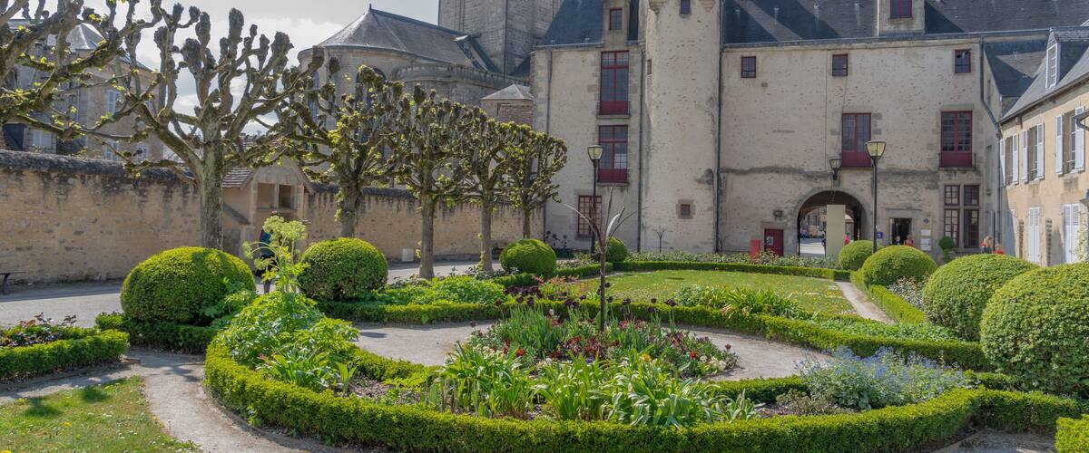 A historic courtyard with manicured hedges, a cactus tree, and a building with a tower.