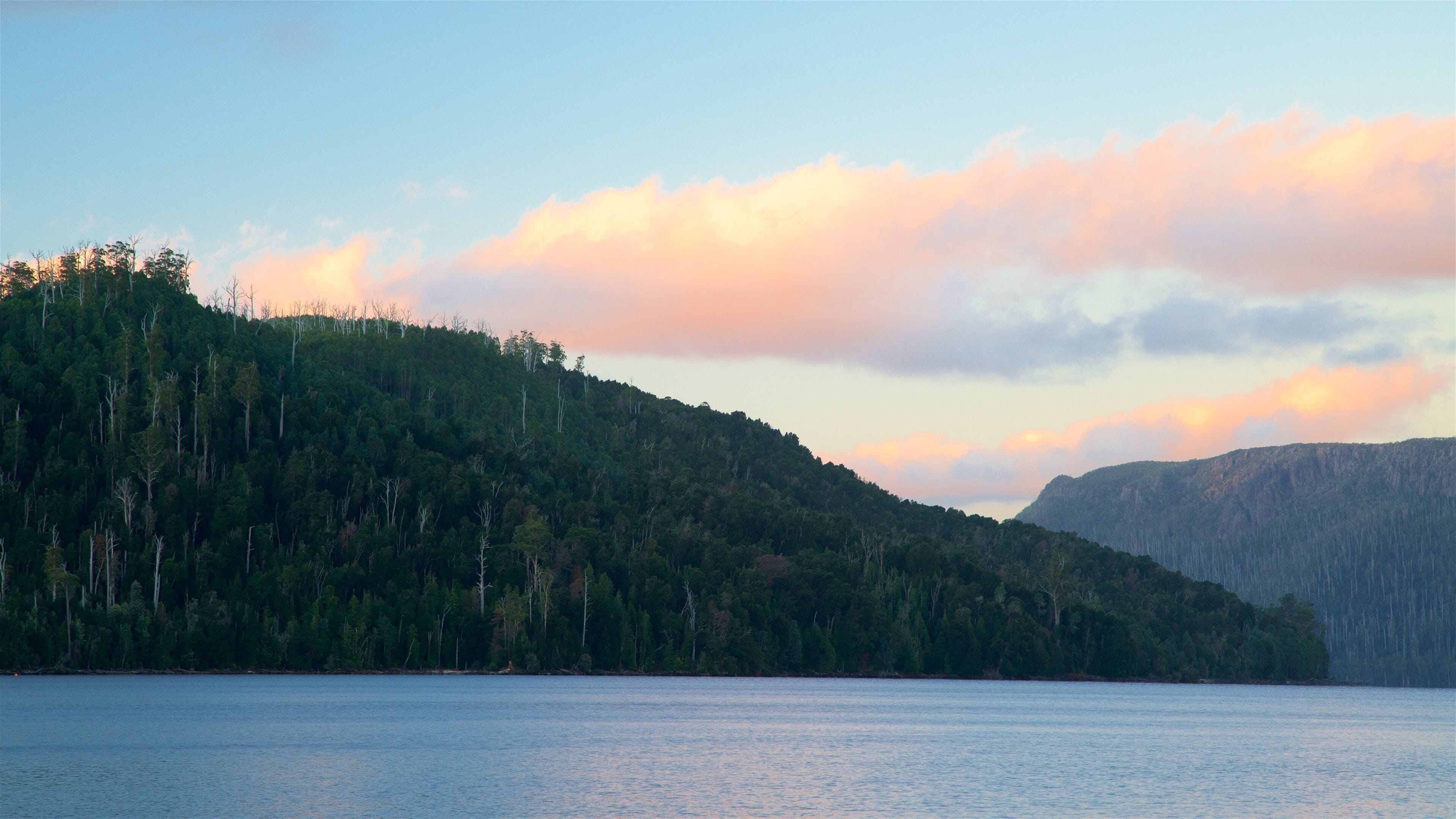 A calm lake surrounded by dense forested hills and a mountain range.
