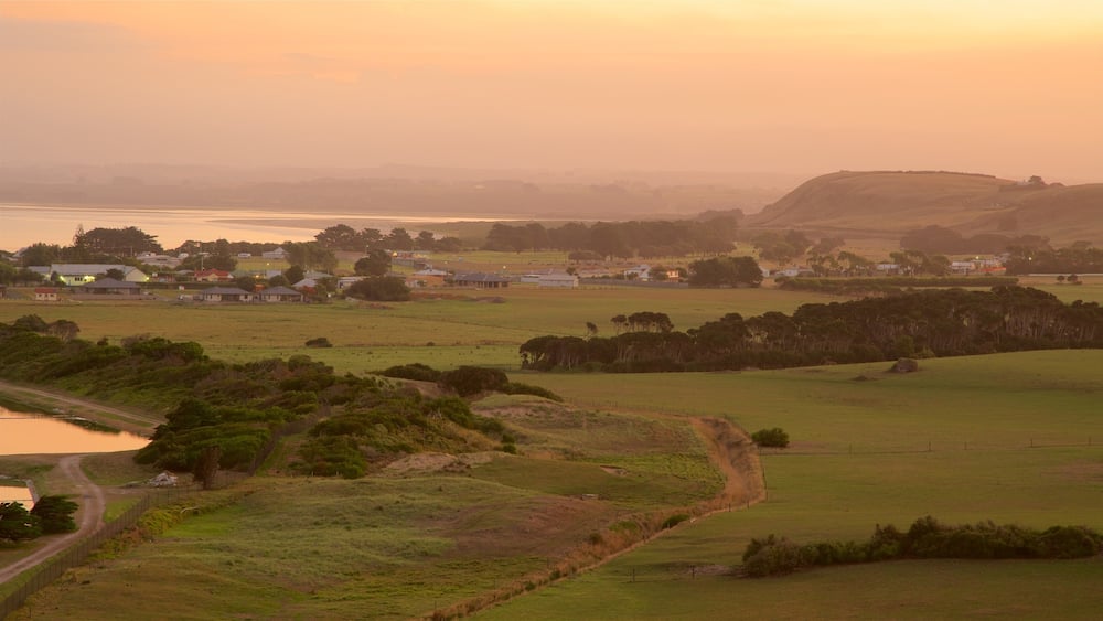 A rural landscape with rolling hills, a small body of water, and scattered houses.