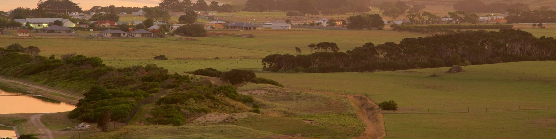 A rural landscape with rolling hills, a small body of water, and scattered houses.