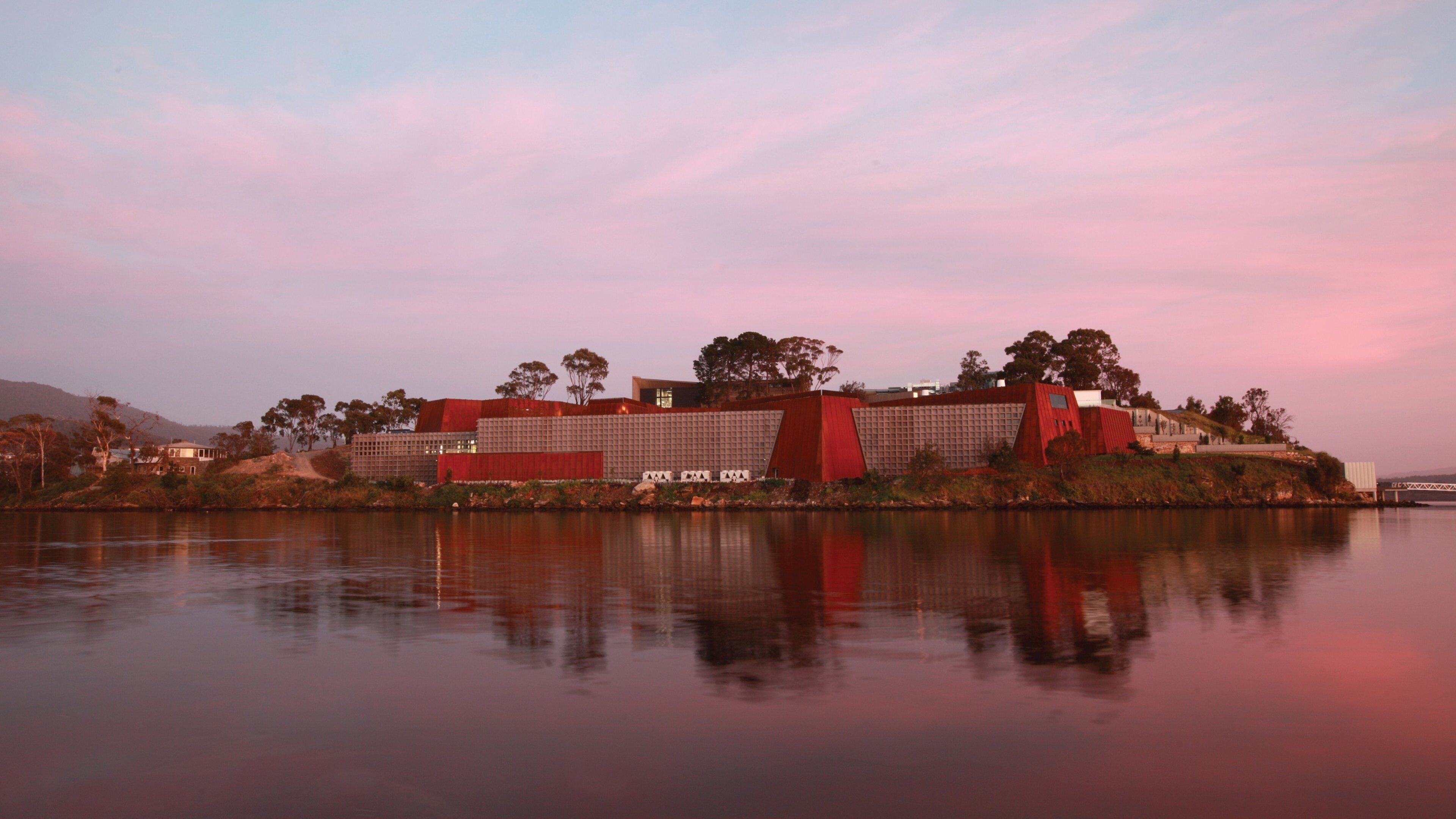 Un moderno complejo de edificios junto a un lago tranquilo, con un cielo rosado.